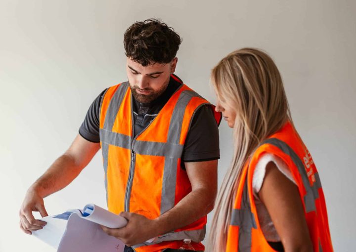 Personeel met een oranje bouwhestje aan het overleggen over papieren - goede werkgever - demt-flex