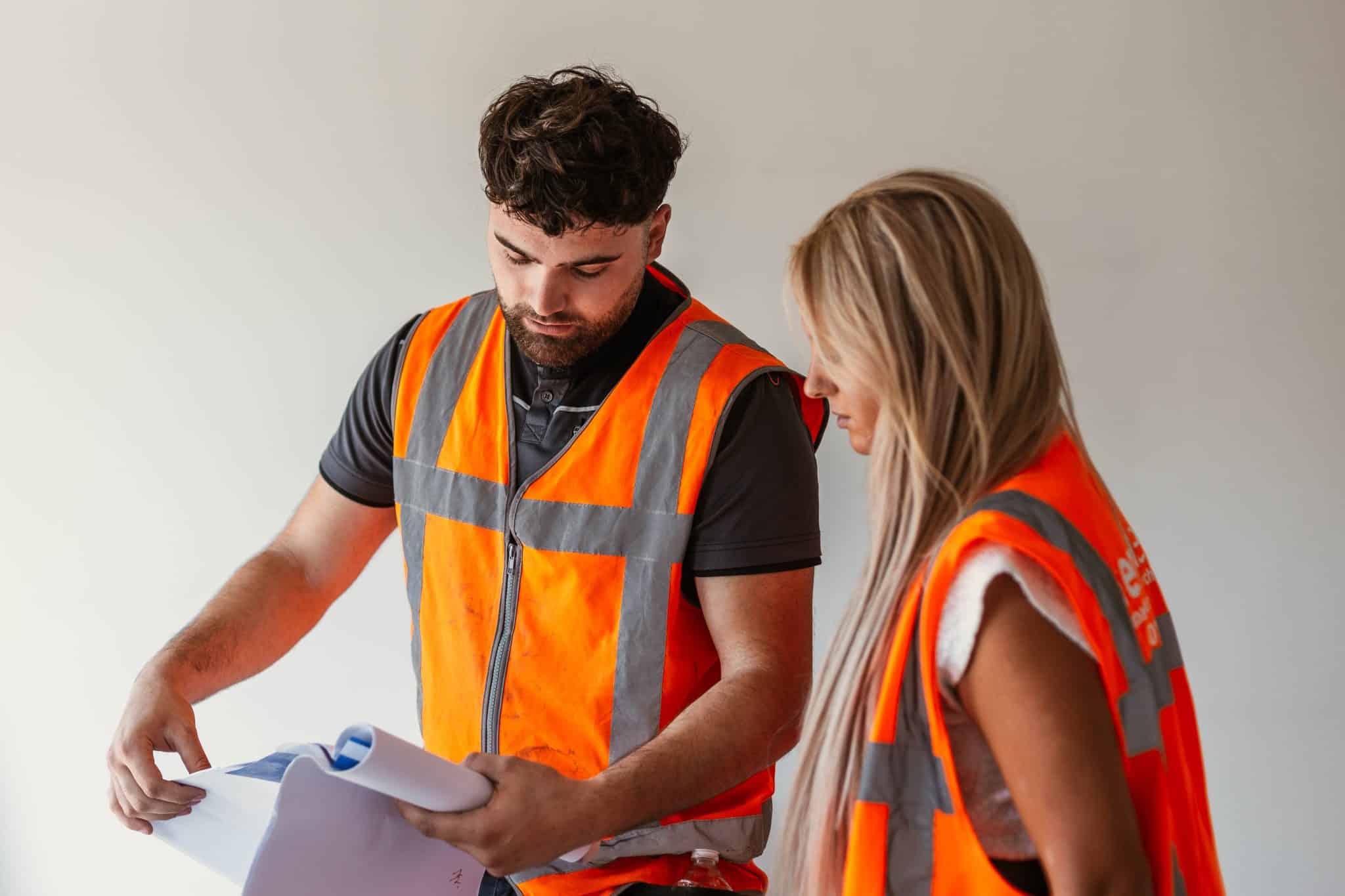 Personeel met een oranje bouwhestje aan het overleggen over papieren - goede werkgever - demt-flex